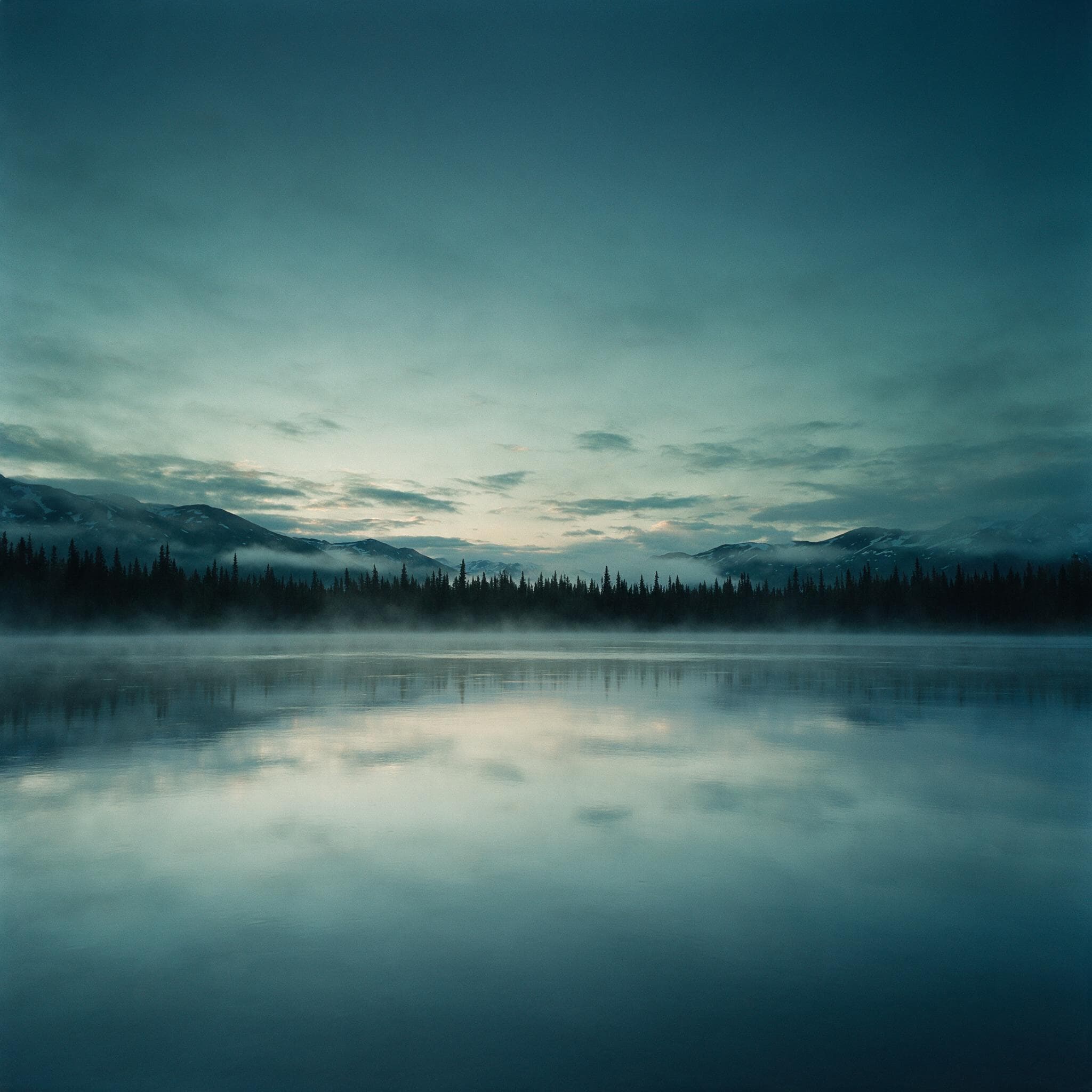 Quiet Alaska water at first light, faint mist over a glassy surface